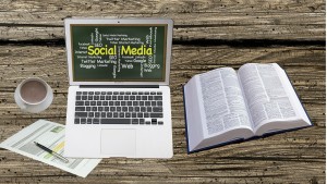 Laptop mit Social Media Tafel auf dem Bildschirm und aufgeschlagenes Buch